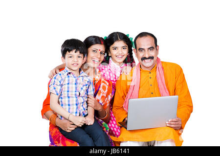 Heureux parents ruraux indiens et 2 enfants assis ensemble et à l'aide d'apprentissage de l'ordinateur portable le développement économique Banque D'Images