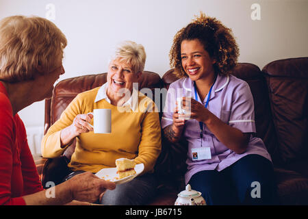 Personne âgée assise avec deux de ses patients dans la maison de soins. Ils profitent d'un peu de gâteau et du thé. Banque D'Images