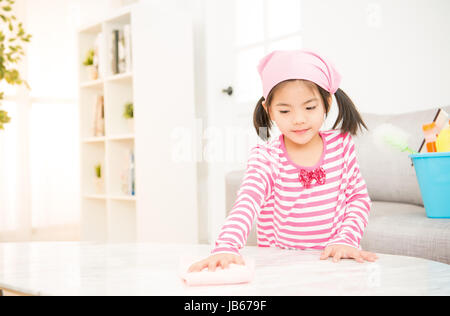 Happy little girl learning chinois asiatique nettoyage avec chiffon dans le salon à la maison. ménage ménage et concept. Banque D'Images