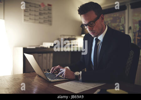 Serious businessman working on laptop la nuit assis dans office à concentrés Banque D'Images