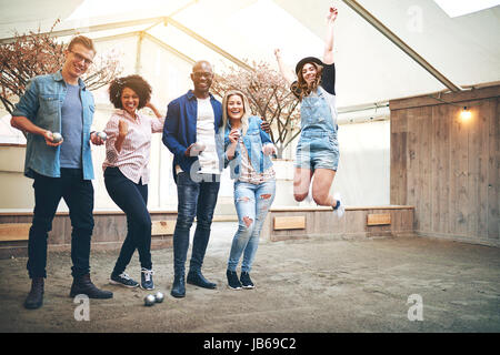 Smiling group des hommes et femmes multiraciales de saut et de tergiversations du plaisir ensemble avec des boules de pétanque. Banque D'Images