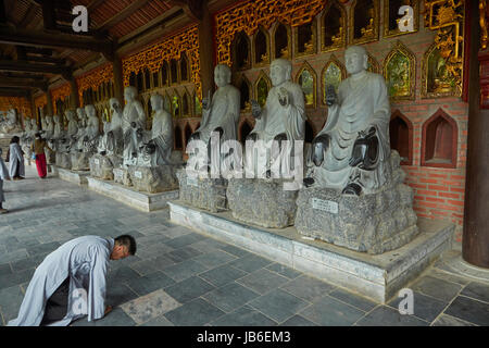 Homme qui prie par rangée de statues Arhat, Bai Dinh Buddist Temple complexe, près de Ninh Binh, Vietnam Banque D'Images