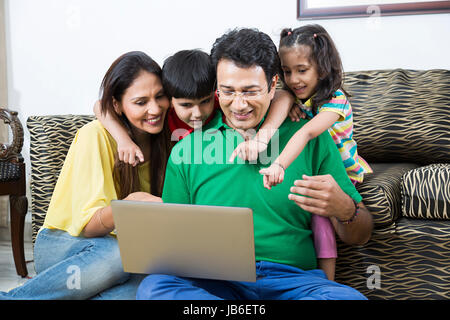 4 personnes à la maison fille enfants parents portable faisant sourire son watching Banque D'Images