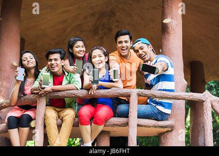 Groupe indien adolescents filles et garçons assis et banc en bois montrant téléphone mobile en park Banque D'Images