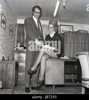 Années 1970, historique, d'un secrétaire portant une mini-jupe est assise sur le bord d'un bureau de son patron qu'elle prend des notes dans son bureau. Banque D'Images