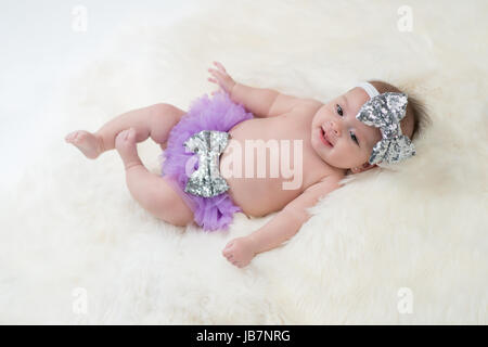 Portrait d'un bébé de quatre mois girl wearing frilly, violet et argent, un sequin, bow serre-tête. Tourné en studio sur un tapis en peau de mouton. Banque D'Images