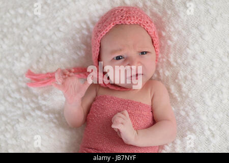 Une semaine trois vieux Naissance bebe Fille portant un bonnet de couleur pêche. Elle est couchée sur un livre blanc, bouncle couverture et a une drôle d'expression sur son visage. Banque D'Images