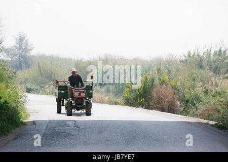 Vieil homme agriculteur sur un très vieux véhicule tracteur sur une route sur une journée ensoleillée Banque D'Images