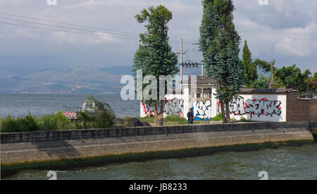 Garé pick up van et l'homme pêche, avec graffitti sur mur derrière sur la propriété à côté du lac Er Hai, Yunnan, Chine Banque D'Images