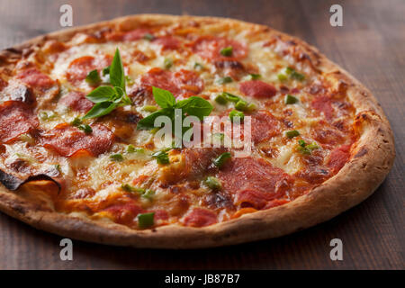 Pizza italien rustique avec pepperoni, poivrons verts, de mozzarella et de feuilles de basilic Banque D'Images