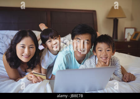 Famille heureuse de faire les achats en ligne sur l'ordinateur portable dans le lit Chambre à la maison Banque D'Images