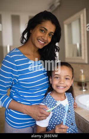 Portrait of smiling girl holding mère avec des brosses à dents dans la salle de bains Banque D'Images