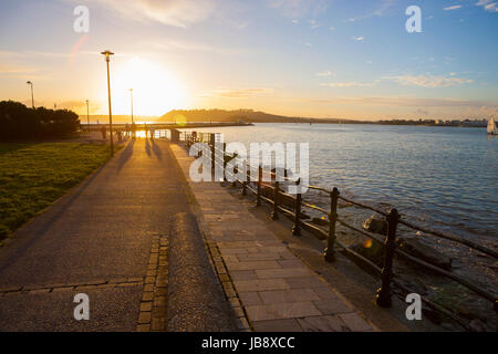 Les adultes autour de la lumière du soleil casting de longues ombres à la fin de la jetée promenade à côté de l'océan de l'eau au coucher du soleil Banque D'Images