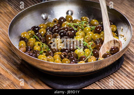 Les olives et le thym dans une poêle avec une cuillère de bois Banque D'Images