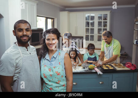 Couple smiling at camera while preparing dessert les membres de la famille en arrière-plan à la maison Banque D'Images