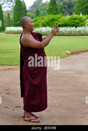 Un moine bouddhiste en robes marron signifie prendre une avec son téléphone portable selfies dans un parc du Myanmar Banque D'Images