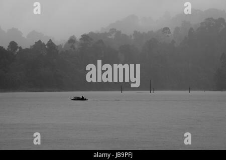 Un petit bateau naviguant sur le lac Cheow Lan dans une pluie tropicale (noir et blanc) Banque D'Images