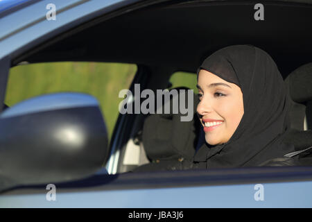 Heureux l'arabie arabe femme conduire une voiture en souriant avec un foulard Banque D'Images