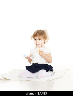 Peu jolie fille est assise sur le sol avec une brosse à dents et coller sur un fond blanc. Banque D'Images