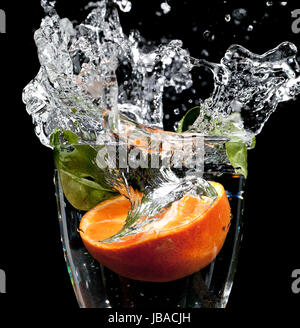 Orange est tombé dans un verre d'eau avec grande éclaboussure figée dans le temps, sur un fond noir Banque D'Images