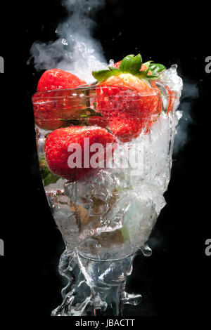 Verre à cocktail de fruits avec de la vapeur et de la fumée, et le mouvement de l'eau gelé, le tout sur un fond noir Banque D'Images