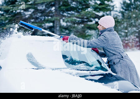 Femme enlever la neige à partir d'une voiture avec un balai après le Blizzard Banque D'Images