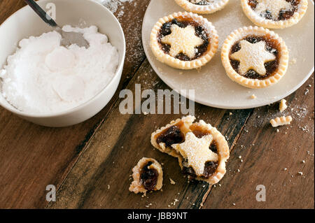 Manger de délicieux petits pâtés de Noël fraîchement décorée avec des étoiles de la pâtisserie et saupoudrée de sucre glace, la moitié mangé pie de miettes dans l'avant-plan Banque D'Images