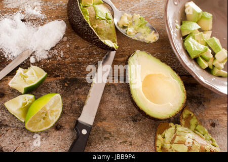 Préparer une délicieuse salade d'avocat frais d'avocat la moitié d'un côté d'un bol avec pelé et coupé en dés, la pâte avec un couteau, de sel et de jus de citron sur une vieille table en bois, vue du dessus Banque D'Images