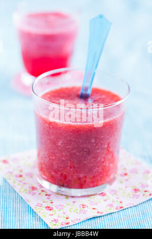 Smoothie aux fraises de gros plan en verre reposant sur serviette floral sur nappe bleu clair avec un autre en arrière-plan Banque D'Images