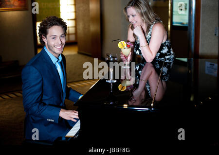 Beau jeune homme jouant du piano et son compagnon divertissant holding cocktail. Couple amour Banque D'Images