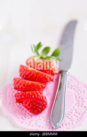 Libre de fraises fraîches, tranchées avec couteau en métal argenté reposant sur le tapis rose décorative Banque D'Images