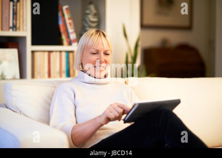 Portrait de vieille femme à l'aide de tablet pc et souriant, assis sur le canapé à la maison Banque D'Images