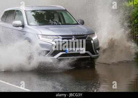 Spray de route en mouvement 2017 Mitsubishi Outlander 5HS PHEV CVT SUV voiture électrique conduisant sur des routes inondées à Tarleton, Lancashire, Royaume-Uni. UK Météo. Inondations après pluie torrentielle rendant difficile la conduite. Après une forte averse, la visibilité était extrêmement limitée, avec des flaques d'eau, de l'eau de surface et un risque d'aquaplaning, avec une perte conséquente de traction et de réaction de la direction. Banque D'Images