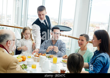 Jeune serveur desservant grande famille pendant le dîner ou le petit déjeuner Banque D'Images