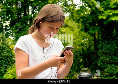 Young woman with smart phone et casque à l'extérieur dans le jardin s'amuser. Banque D'Images