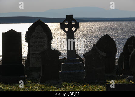 Vue sur Lamb Holm du cimetière de l'église Saint-Nicolas sur le continent, l'Orkney : une croix celtique et pierres tombales sont découpé sur Holm Sound. Banque D'Images