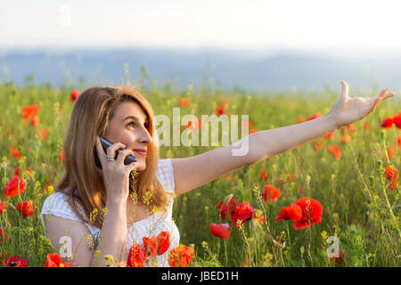 Young Girl wearing white dress cloth debout dans un champ de coquelicots à parler au téléphone Banque D'Images