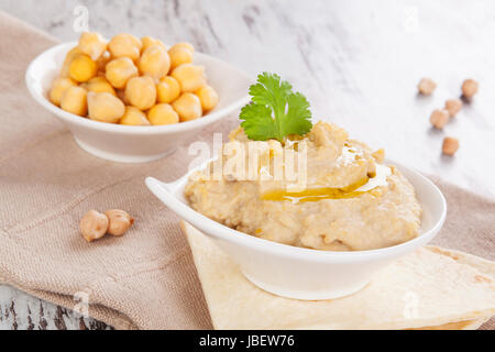 L'hummus délicieux cuit et les pois chiches dans un bol blanc sur fond de bois. L'hummus culinaire méditerranéenne de manger, de style rustique. Banque D'Images