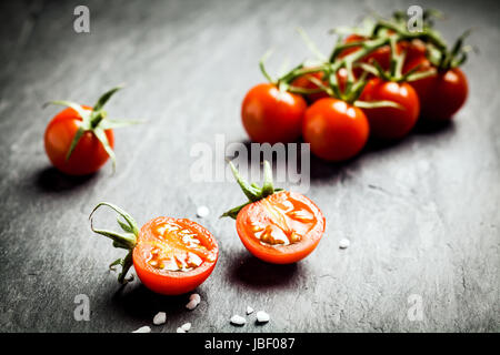 Moitié de tomates raisin frais mûrs montrant les pépins et la pulpe juteuse au premier plan avec un tas de tomates sur la vigne derrière sur une table rustique, low angle avec copyspace Banque D'Images