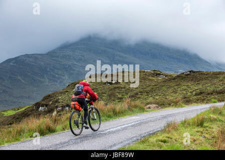 Lonely biker vélo dans les Highlands écossais, lourdement chargé sur vélos de cyclotourisme le long de la route à voie unique dans le mauvais temps pluvieux, Ecosse, Royaume-Uni Banque D'Images