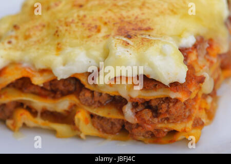 Close-up d'une lasagne traditionnelle faite avec du bœuf haché sauce bolognaise garnie de feuilles de basilic servi sur une plaque blanche Banque D'Images