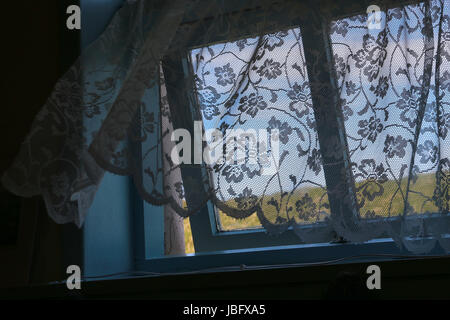 Rideau de dentelle à l'ancienne un souffle une brise marine qui est venu à travers une fenêtre légèrement ouverte ; ciel bleu et vert de l'herbe à l'extérieur un jour de printemps. Banque D'Images