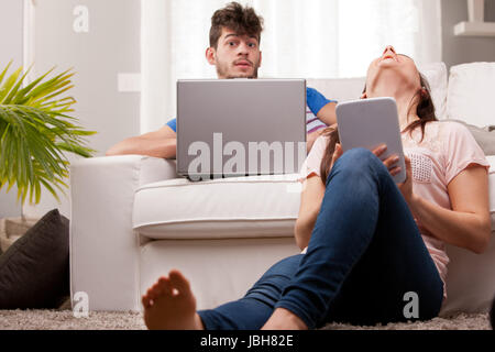 Un homme et une femme à l'aide d'un ordinateur portable et une tablette dans leur salle de séjour Banque D'Images