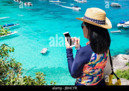 Traveller femme avec maillot coloré utiliser mobile prendre une photo de vue en haut de la montagne et de la mer en bateau de vitesse,les vacances d'été en voyage. Banque D'Images
