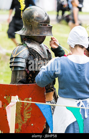 Dans l'article de chevalier armure médiévale étant donné une boisson par un long tube tenu par une femme vêtue de vêtements médiévaux. Reconstitution d'un événement d'histoire vivante. Banque D'Images