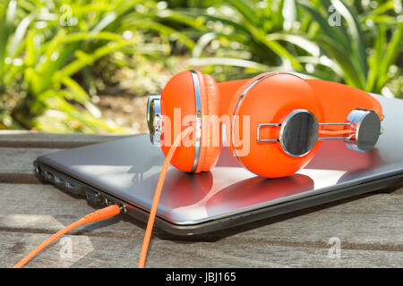 De couleur orange vif et casque ordinateur mobile sur le banc dans le parc Banque D'Images