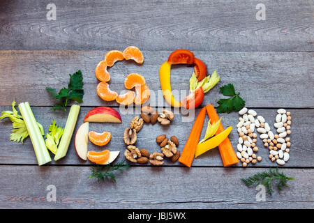 Mots 'Go vegan" écrit avec légumes, fruits, noix et légumineuses sur fond de bois rustique, concept - ingrédients biologiques pour une alimentation végétalienne saine Banque D'Images