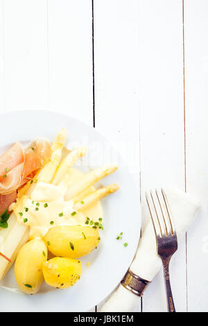 Asperges Blanches avec prosciutto jambon et pommes de terre bouillies bébé garni de mayonnaise crémeuse servi sur une table en bois blanc peint rustique avec copyspace Banque D'Images