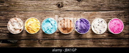Ligne d'un assortiment de saveurs et les couleurs de la crème glacée italienne gastronomique servi dans des bains à remous à emporter en plastique sur une table en bois rustique, format bannière horizontale avec copyspace Banque D'Images