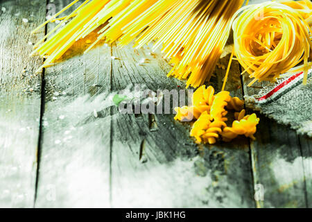 Variété de pâtes séchées italiennes ingrédients disposés dans l'angle sur les planches de bois avec météo rustique copyspace y compris spaghetti, fusilli , tagliatelli et linguini Banque D'Images